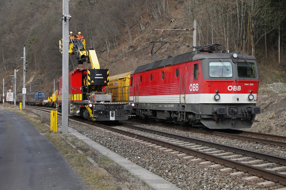 1144 250 zieht am 2.03.2016 einen Güterzug zwischen Bruck/Mur und Pernegg Richtung Süden. Am Nachbargleis wird gerade eine neue Fahrleitung montiert.