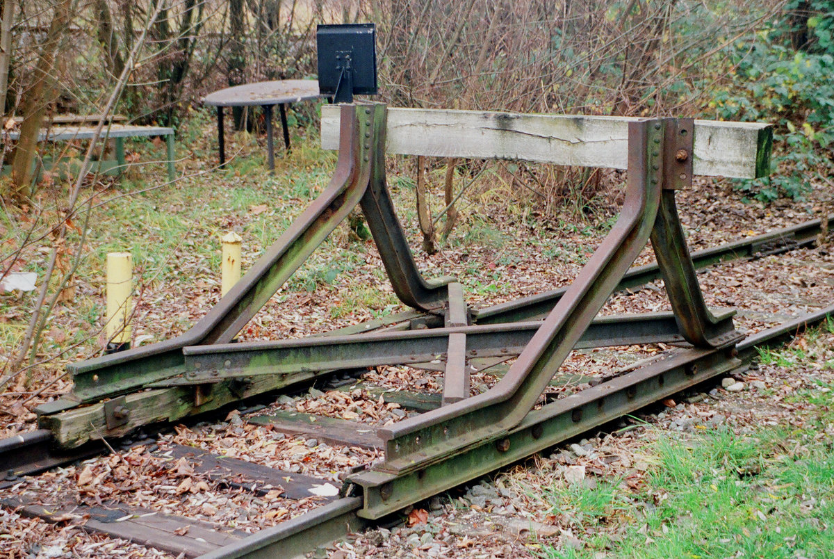 12. November 1996, Freilassing, Prellbock am südlichen Ende des parallel zur Mühldorfer Strecke verlaufenden Industrieanschlussgleises. In der wärmeren Jahreszeit haben meine Kollegen und -innen auf den  Möbeln  im Hintergrund ihre Pausen genossen.