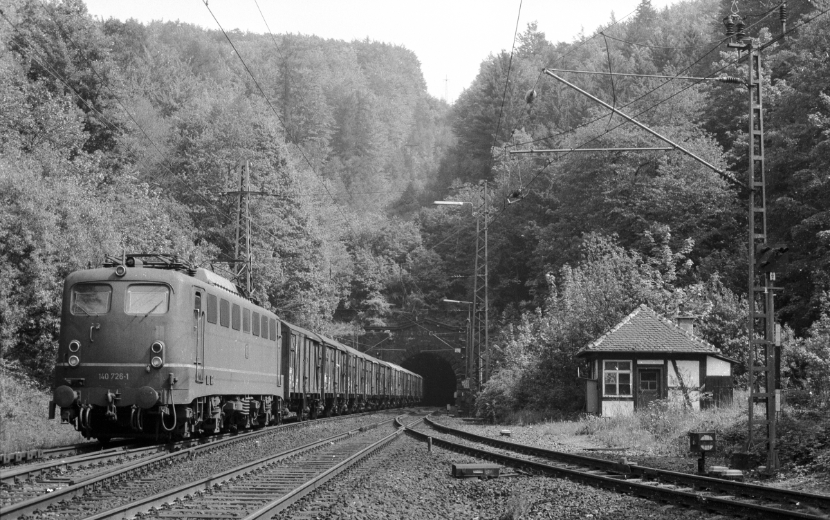 140 726 mit einem Güterzug komplett aus zweiachsigen EUROP-Einheitsgüterwagen verlässt den Heigenbrückener Tunnel (10.8.1981). Rechts das Schiebelok-Wartegleis.