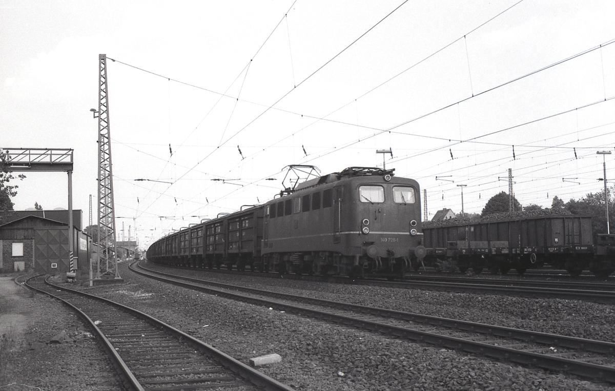 140726 ist am 3.9.1985 mit einem Güterzug in Richtung Münster unterwegs.
Hier bei der Durchfahrt in Hasbergen sieht man links noch den alten Ladekran und die Verladehalle der Amazonen Werke. Beide sind inzwischen längst abgerissen worden.