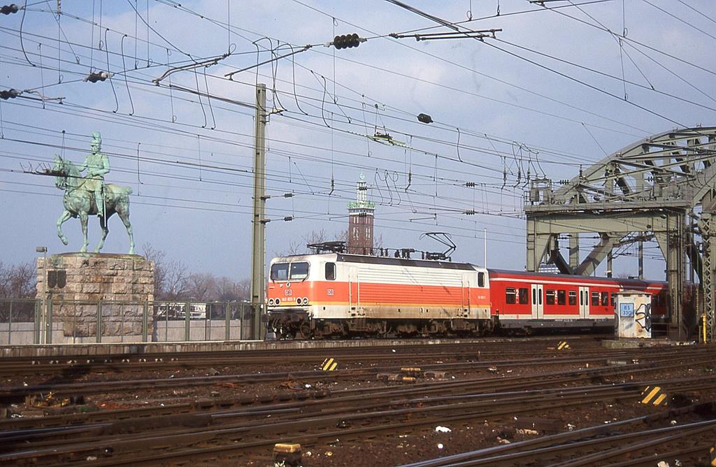 143823 in orangener S-Bahn Lackierung verläßt hier am 24.3.1999 um 16.50 Uhr die Hohenzollernbrücke in Köln und erreicht den HBF Köln.