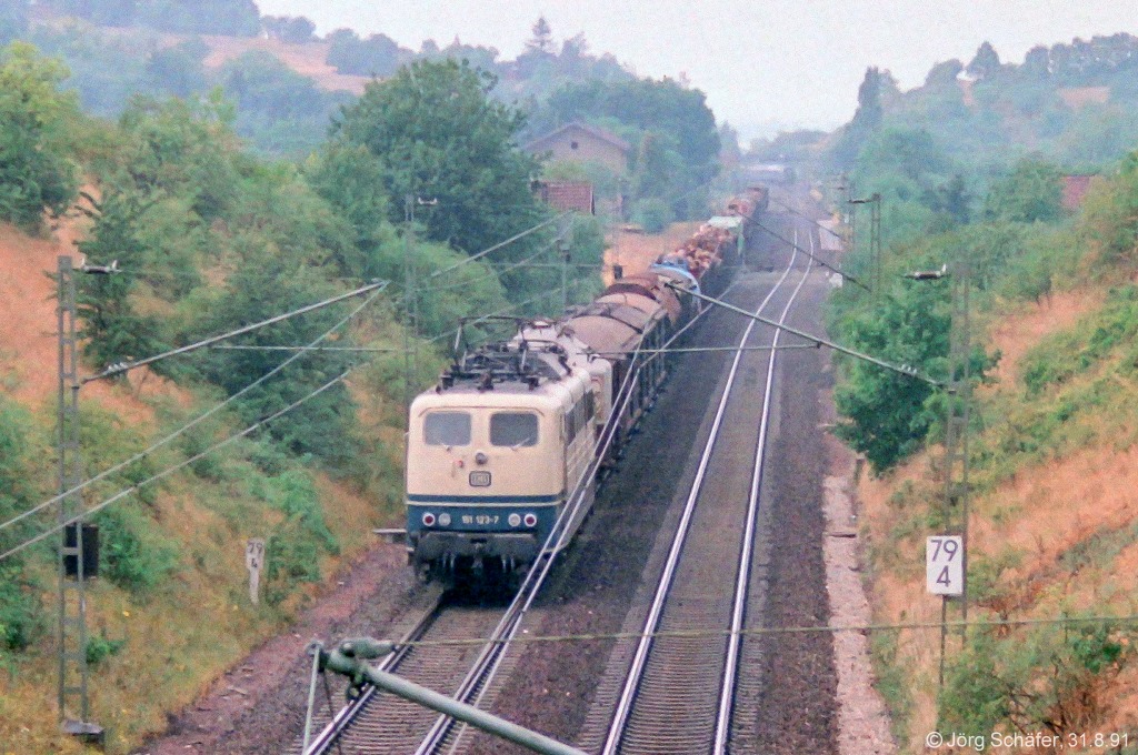 151 122 war am 31.8.91 mit einem Güterzug Richtung Ansbach südlich von Burgbernheim bei km 79,4. Im Hintergrund sieht man noch die Gleisaufweitung für den alten Inselbahnsteig neben Gleis 2. 