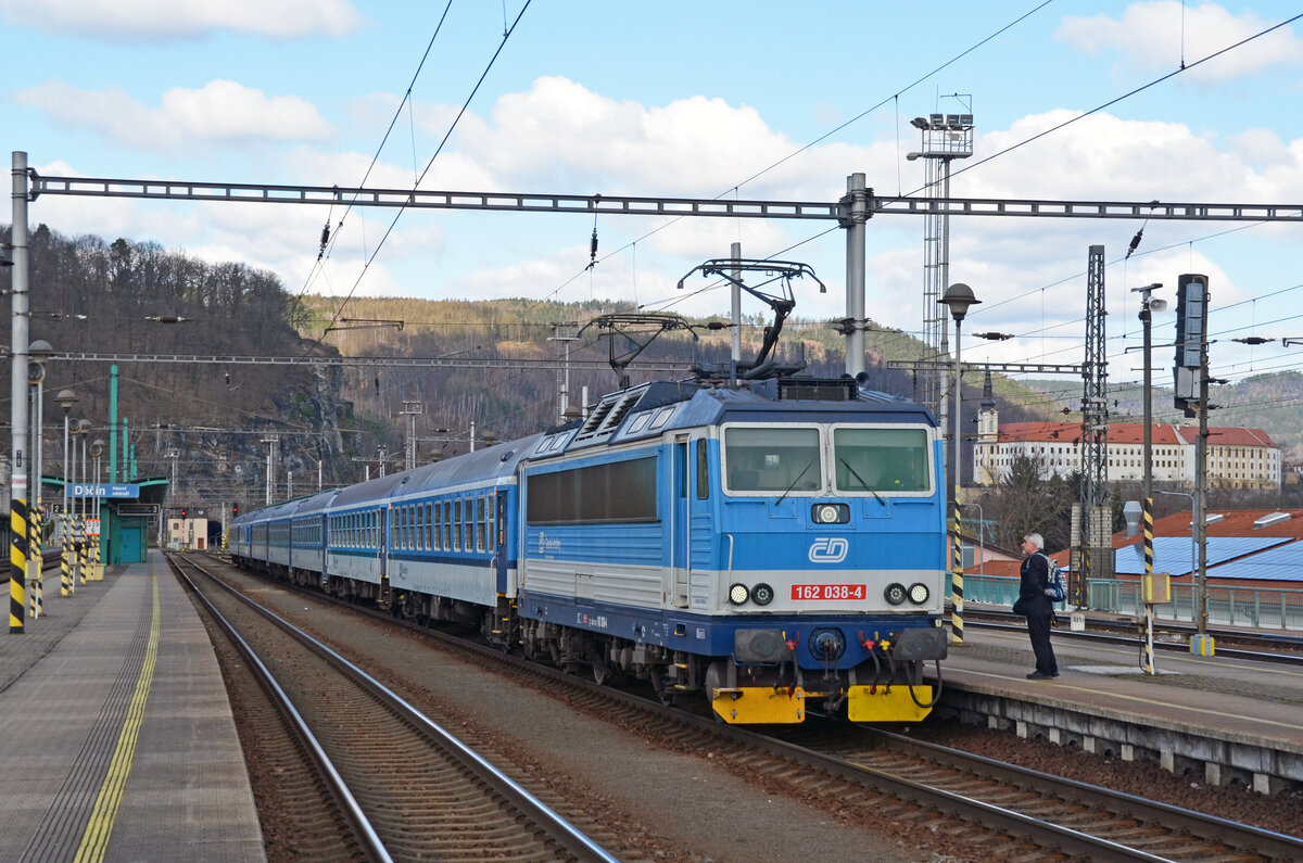 162 038 wartet am 01.04.25 in Decin mit ihrem R 689 auf die Abfahrt nach Praha. Rechts ist das Schloss Decin zu sehen.
