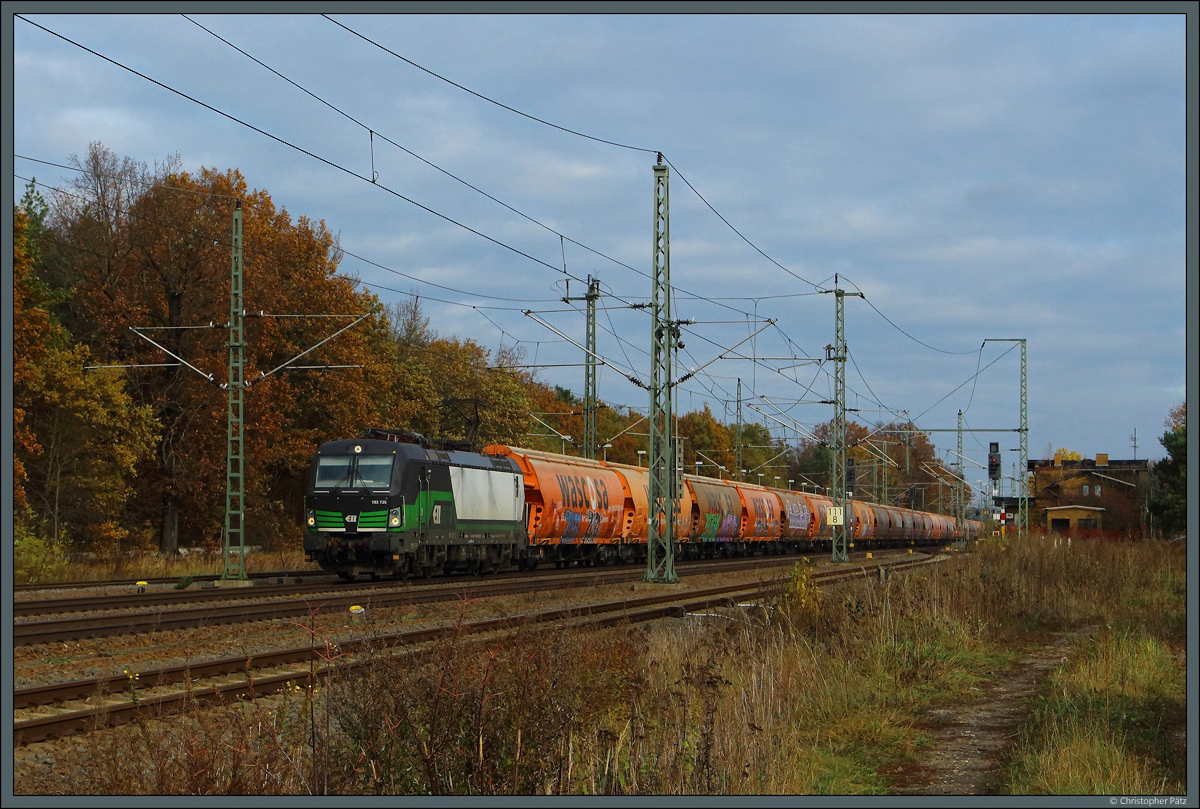 193 735 der ELL rollt mit einem Schüttgutzug am 06.11.2021 durch den Bahnhof Radis. Rechts ist das ehemalige Empfangsgebäude zu erkennen.