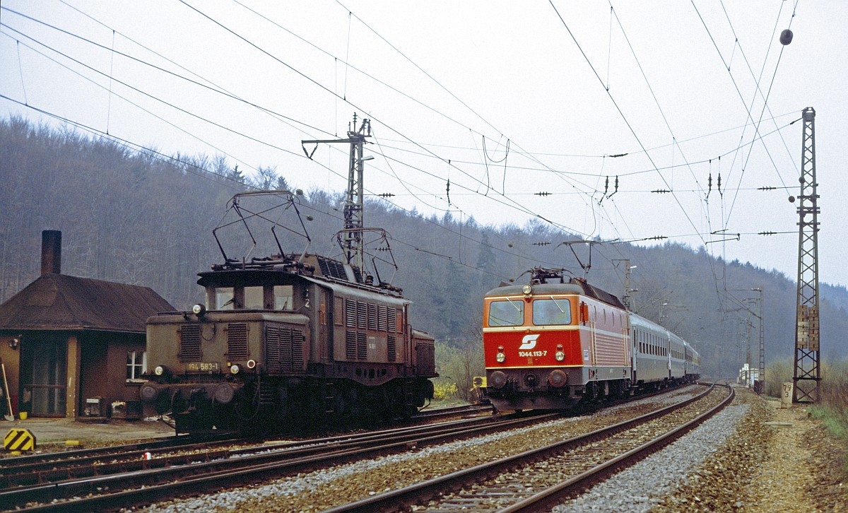 194 583, auf neue Aufgaben wartend, wird von ÖBB 1044.113 vor D 251 Frankfurt - Prag überholt (Laufach, 19.4.1987). 