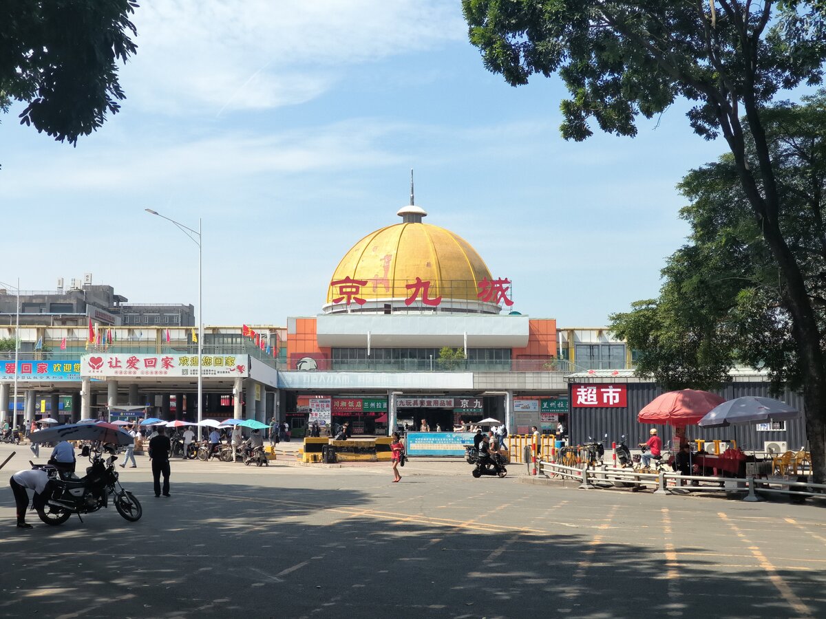2024.10.13,  Jing-Jiu (Railway) City , next to DongGuan East Station. Despite the very railway-ish name (describing the BeiJing---Kowloon Railway next to it), a classic Chinese Station Nameboard-ish font (big red, default font), it was more like a shopping mall or a big market opened right next to the actual station. All sorts of small business opened here, keeping the station itself clean.
///
2024.10.13, „Jing-Jiu (Railway) City“, neben dem Ostbahnhof DongGuan. Trotz des sehr eisenbahnähnlichen Namens (der die benachbarte BeiJing-Kowloon-Bahn beschreibt) und der klassischen chinesischen Schriftart für die Bahnhofstafel (große rote Standardschrift) war es eher ein Einkaufszentrum oder ein großer Markt, der direkt neben dem eigentlichen Bahnhof eröffnet wurde. Alle Arten von kleinen Geschäften eröffneten hier und hielten den Bahnhof selbst sauber.
