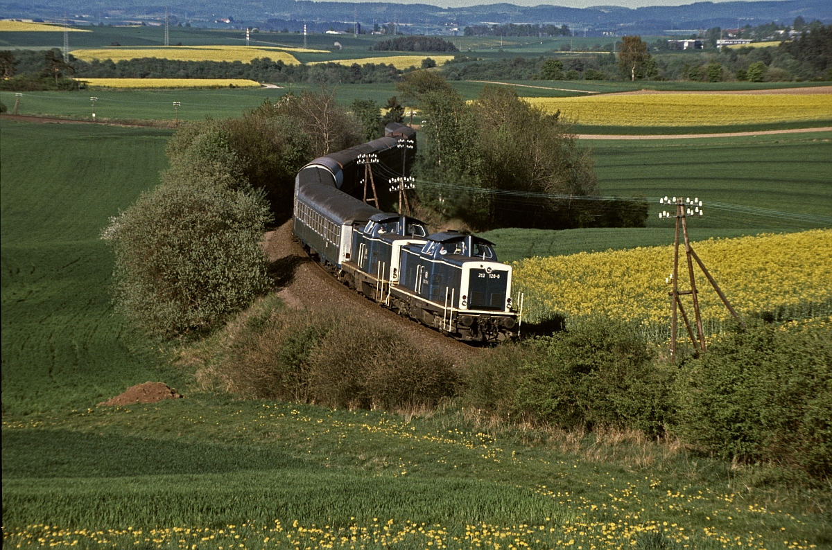 212 128 und eine Schwestermaschine in der fotogenen S-Kurve vor dem Bahnhof Birkenbringhausen. Der Zug, der wie ein Gmp aussieht ist Üg 69005 von Frankenberg nach Marburg, der planmäßig leere Reisezugwagen nach Marburg zurückführte (Mai 1983).