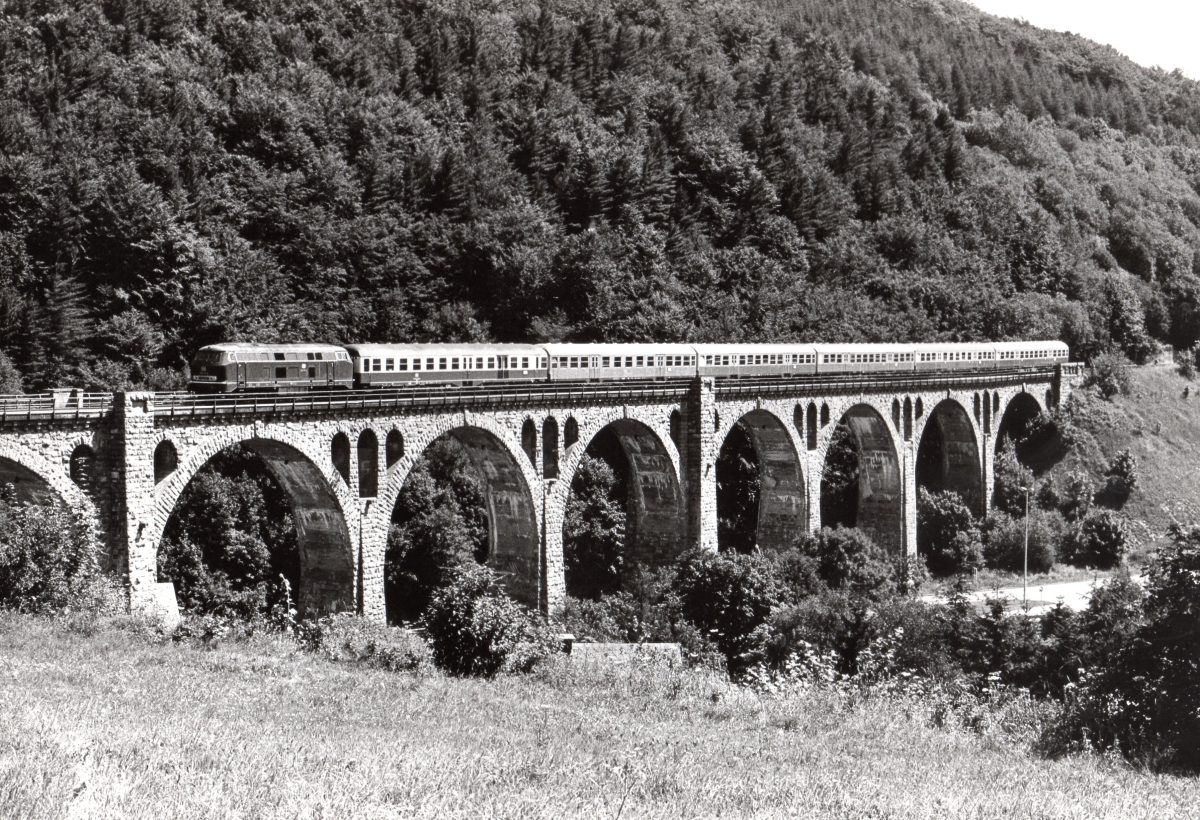 216 102 vom BW Kassel führt E 3598 Marburg-Altenbeken über das Willinger Viadukt im Mai 1984. Die letzen zwei Silberlinge sind Kurswagen von Bad Wildungen nach Köln. Bei der Zuglänge werden Erinnerungen an den klassischen  Heckeneilzug  Frankfurt - Bremen wach, der in ähnlicher Zeitlage das Upland durchfuhr, aber zum Zeitpunkt dieser Aufnahme schon einige Jahre Geschichte war. Man beachte auch, dass das Viadukt noch seine Natursteinverblendung trägt, die später sanierungsbedingt mit Beton  überspritzt  wurde. 