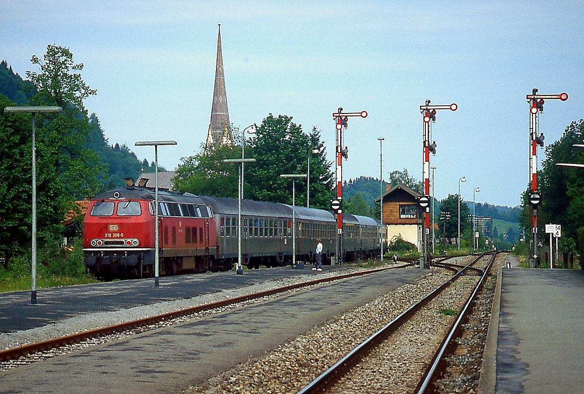 218 308-5 verlässt im Frühjahr 1991 den Bahnhof Schliersee in Richtung Bayrischzell, geradeaus geht es nach München. Zu diesem Zeitpunkt wurde Gleis 2 nicht regelmäßig genutzt, die drei charakteristischen Ausfahrsignale stehen noch.