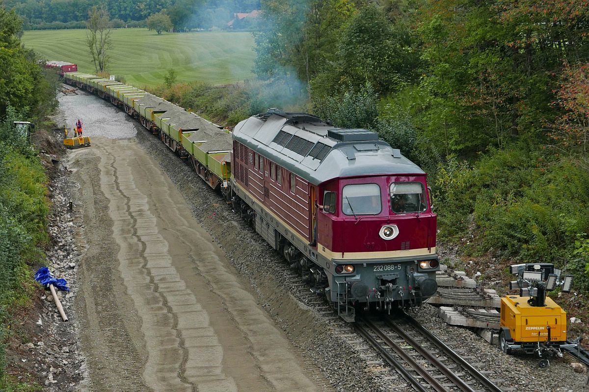 232 088-5 der Salzland Rail Service brachte am 22.09.2020 mit Sand befüllte Kippmulden auf Tragwagen der Gattung Sgns und Schotter mit Schüttgutkippwagen der Gattung Fans zur Gleisbaustelle in der Nähe von Meckenbeuren (bei Lohner), wo bereits ein Gleisbett unter einer Brücke tiefergelegt wurde, damit später die Oberleitung durchgeführt werden kann.