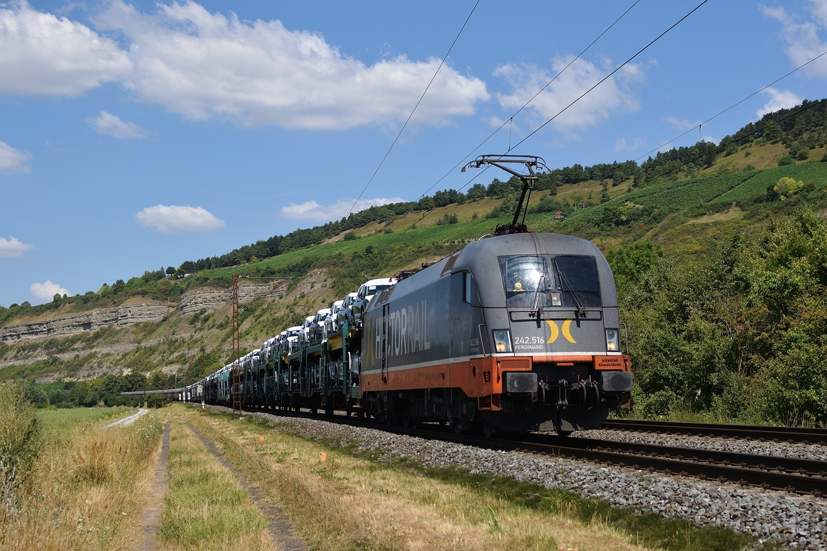 242 516 von Hectorrail zieht am 26. Juli 2018 einen mit Autos beladenen Zug kurz vor Thüngersheim Richtung Würzburg.