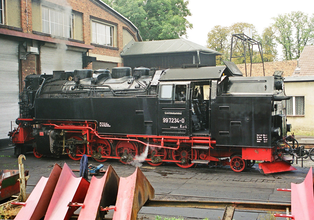 29. Juli 2003, im Bw Wernigerode-Westerntor der Harzer Schmalspurbahn steht Lok DR 99 7234 vor dem Schuppen. Die Schneeräumer im Vordergrund könnten Symbolcharakter haben: Diese Lok war am 08. Januar 2019 kurz vor Erreichen des Brockens im Schnee stecken geblieben und musste mit viel  Manpower  geborgen werden. Für den Schlepp des Zuges und der Lok ins Tal sah man Fotos von 99 232 und 99 240 in den Medien.