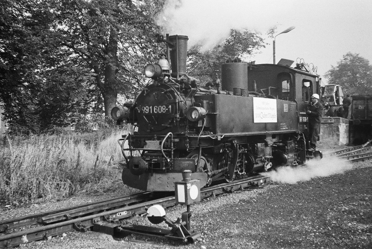 29. September 1984, Schmalspurbahnhof Mügeln. Die Mügelner Schmalspurbahn feierte an diesem Wochenende ihr 100-jähriges Bestehen. Gleichzeitig konnte die Stadt Mügeln auf eine 1000-jährige Geschichte zurückblicken. Verschwiegen wurde auch nicht, dass auch die DDR ein rundes Jubiläum feierte, sie wurde vor 35 Jahren gegründet. Schilder und Fähnchen wiesen an den Lokomotiven auf diese Ereignisse hin. Lok 99 608 rangiert.