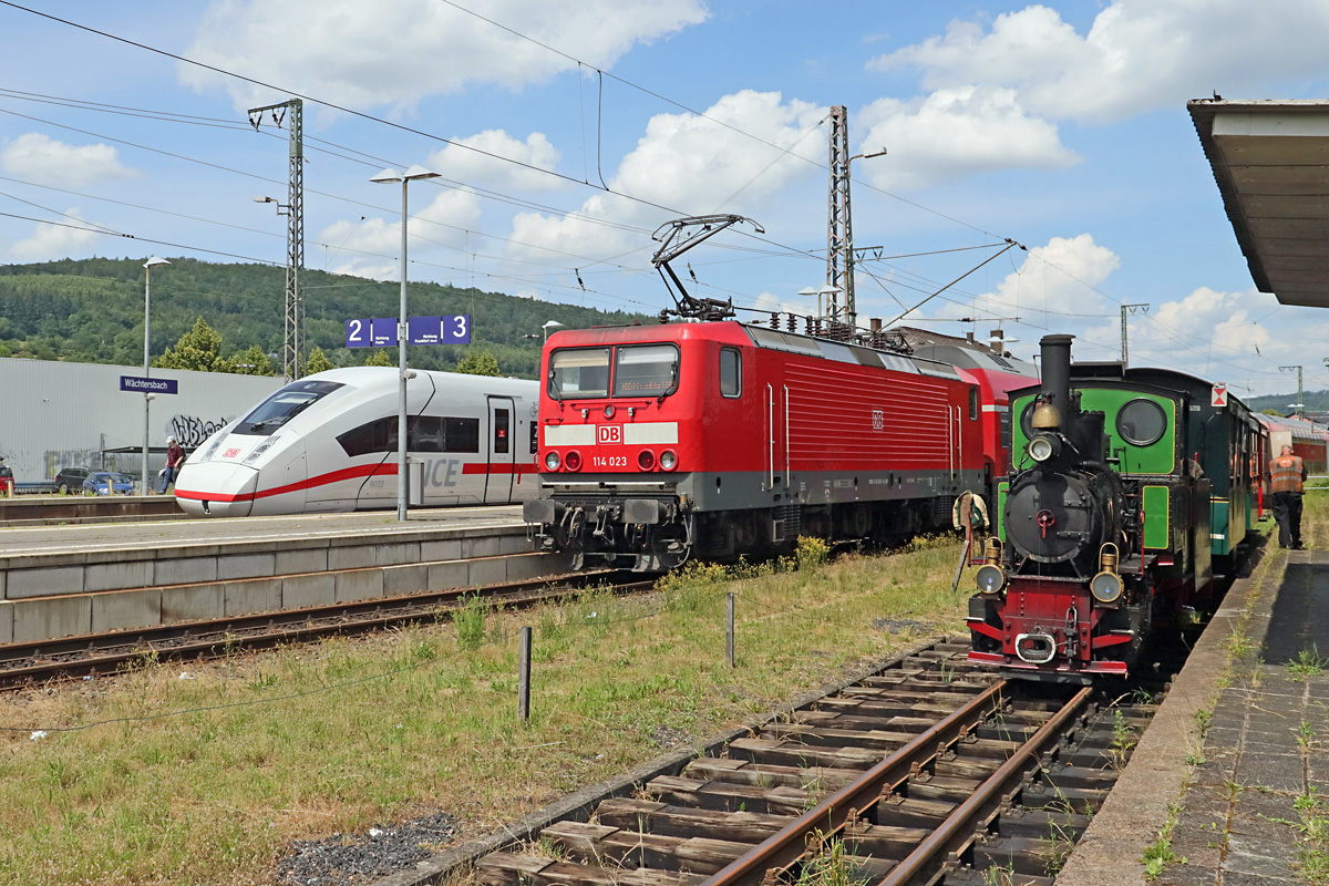 3 sehr unterschiedliche Züge im Bahnhof Wächtersbach am 27.06.2021. Während die Lok  Emma  der Dampfkleinbahn Bad Orb für die Rückfahrt nach Bad Orb schon umgesetzt hat, muss die 114 023 dieses Manöver nicht bewerkstelligen. Sie hat den RB 15518 aus Frankfurt(Main) nach Wächtersbach geschoben und verbleibt für die Rückfahrt als RB 15521 an der Spitze des Zuges. Nur der Stromabnehmer muß noch gewechselt werden. Der ICE 4 auf dem Nachbargleis hat dagegen keinen Halt, der ist erst in Fulda geplant. 