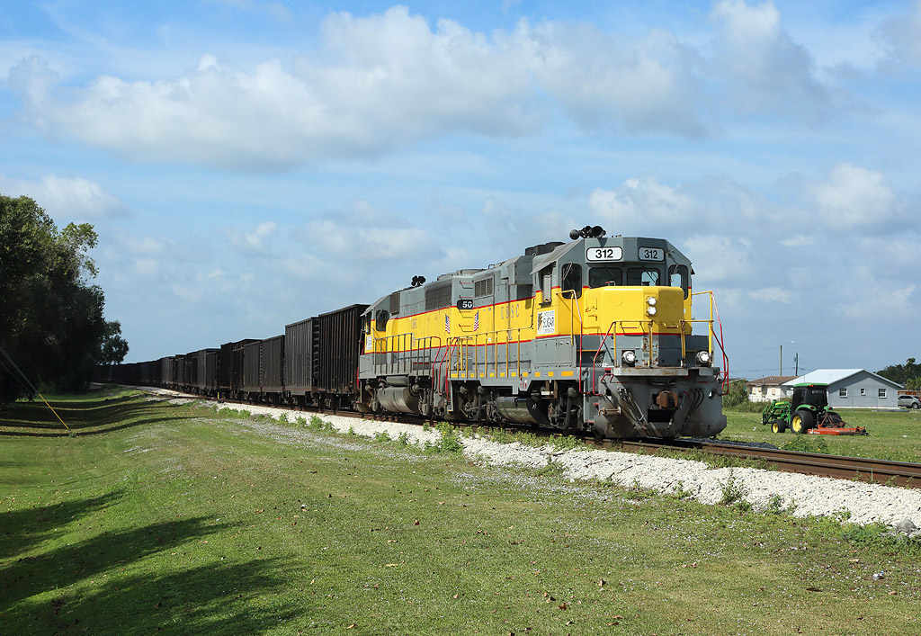 312 passes South Bay whilst hauling BT1, empty sugarcane cars from Clewiston to Bryant, 14 Feb 2020.

506 is being hauled in the consist...