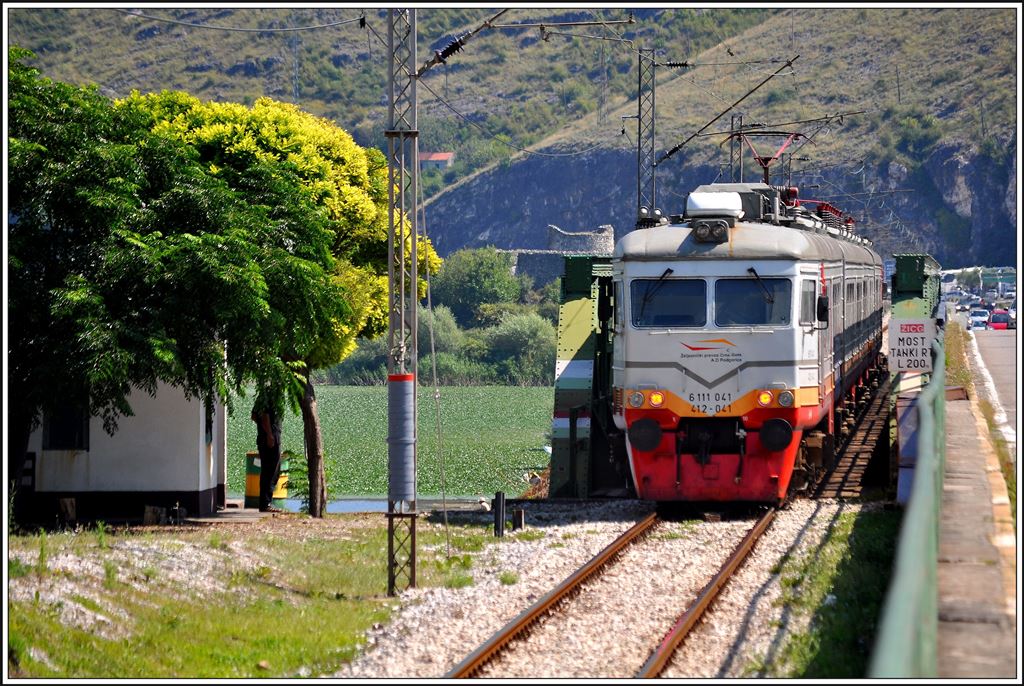 6 111 042/041 als R6152 von Bar nach Podgorica fährt hier auf den Damm von Lesendro am Skadarska Jezero/Skutarisee.Für Schiffe zwischen dem westlichen und östlichen Seeteil gibt es auch eine Brücke für die Bahn und die Strasse. Der idyllisch gelegene Brückenposten ist nach wie vor besetzt, aus welchem Grund auch immer. (11.08.2014)