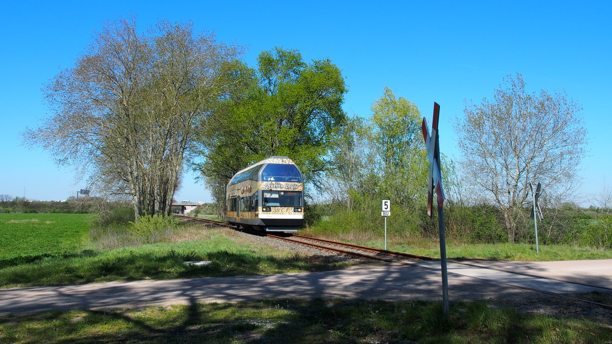 670 003  Fürstin Louise  fährt am Ostermontag des Jahres 2019 dem Ziel Wörlitz entgegen und passiert hier den BÜ kurz vor dem Bedarfshalt  Dessau Adria .
Im Hintergrund ist die A9 zu sehen.

Dessau, der 22.04.2019