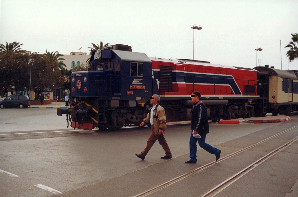 91 91 0000 570-2 (040-GT-570) (Bo'Bo', de, Hersteller: EMD, Type: GT18B, Fab.Nr.: 938830-20 Baujahr 1999) fährt am 02.Jänner 2002 mit dem DC 5-22/59 über den Place Farhad Hached in Sousse. (Fotoscan)