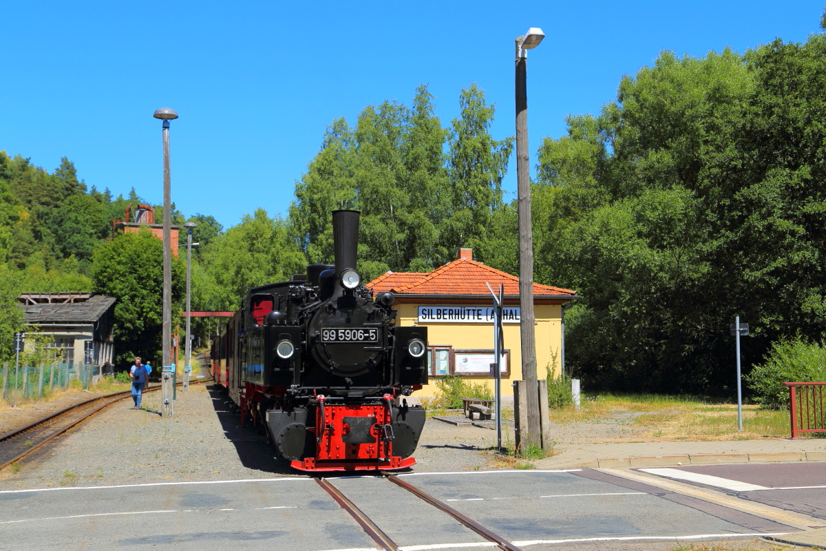 99 5906 mit Jubiläumssonderzug am 07.07.2018 im Haltepunkt Silberhütte. In Kürze wird auf Gleis 2 ein Planzug überholen. Dann setzt der Sonderzug auf Gleis 2 um und wartet auf die Kreuzung mit einem Plantriebwagen. Erst danach kann er seine Fahrt in Richtung Stiege fortsetzen.