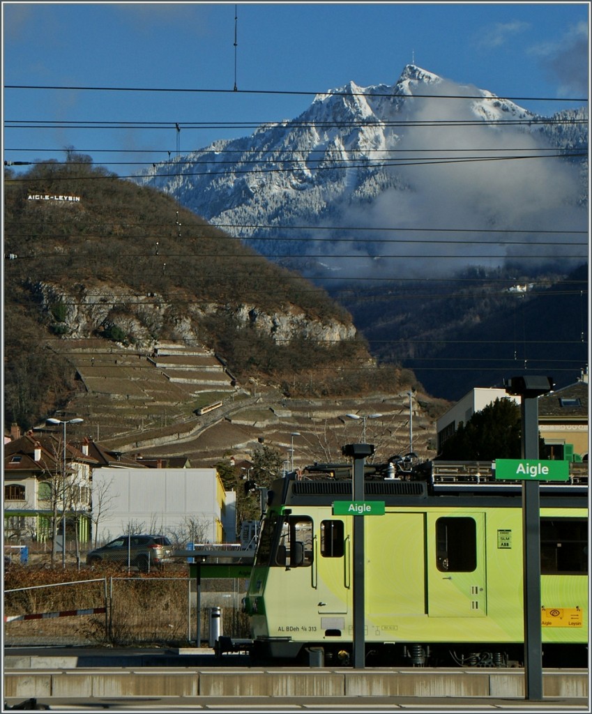 A - L Aigle Leysin: Im Vordergurnd der BDeh 4/4 313 in Aigle, in der Bildmitte zahnt der BDeh 4/4 301 mit Bt 352 Bergwärts und hoch oben am Berg wirbt die A-L schlicht mit Aigle - Leysin. 
5. Januar 2014