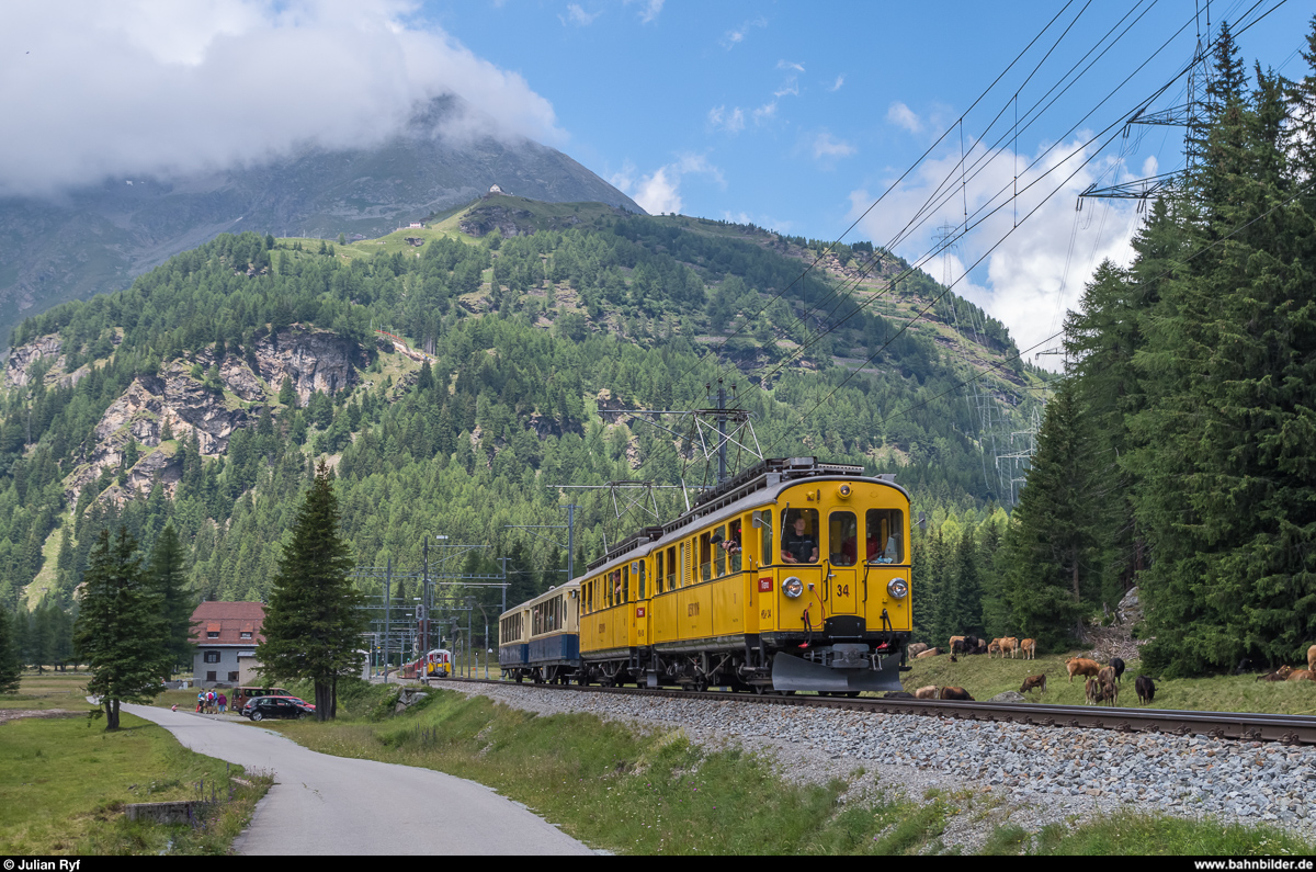 ABe 4/4 34 und 30 verlassen am 12. Juli 2017 die Station Cavaglia. Hoch obendrüber ist im Hintergrund die Alp Grüm mit der Panoramakurve zu erkennen.