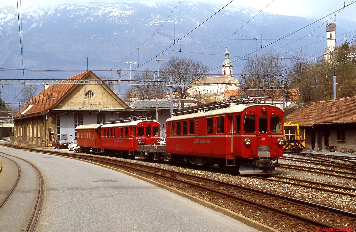 ABe 4/4 I 30 und 32 der Chur-Arosa-Bahn im April 1996 im Depot Chur. Die Fahrzeuge wurden 1911 bzw. 1908 ursprünglich für die Berninabahn gebaut und 1953 bzw. 1946 modernisiert. Da beide Bahnen mit Gleichstrom betrieben wurden (Bernina 1.000 V, Chur-Arosa 2.400 V), wurde in die Triebwagen eine Zweispannungsanlage eingebaut, um sie auf beiden Bahnen freizügig einsetzen zu können. Nach der Umstellung der Chur-Arosa-Linie 1997 auf Wechselstrom wurden die Fahrzeuge hier nicht mehr benötigt. ABe 4/4 I 30 erhielt 2000 die ursprüngliche gelbe Farbgebung zurück und wird heute auf der Berninanbahn als Nostalgietriebwagen eingesetzt, ABe 4/4 I 32 wurde 2009 verschrottet.