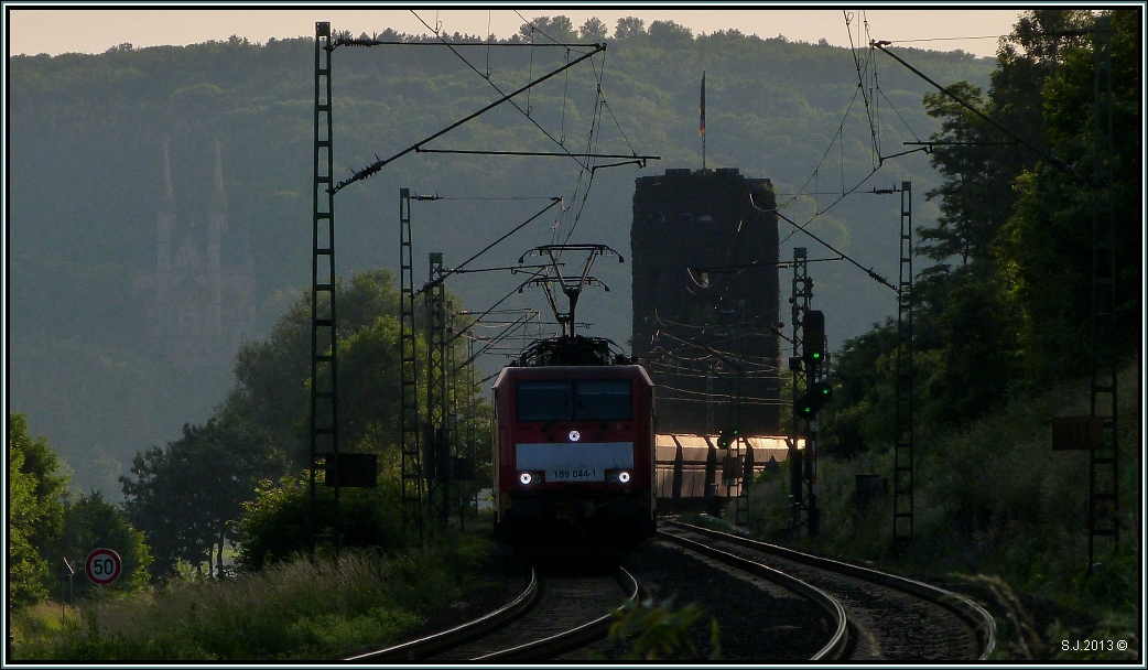 Abendstimmung an der KBS 465 bei Erpel am Rhein im Juni 2013. Ein Erzzug ist gerade unterwegs in Richtung Koblenz. Im Hintergrund ragt der Brckenkopf der alten Remagener Brcke heraus,links im Dunst sticht die Apollinariskirche noch ein wenig hervor.