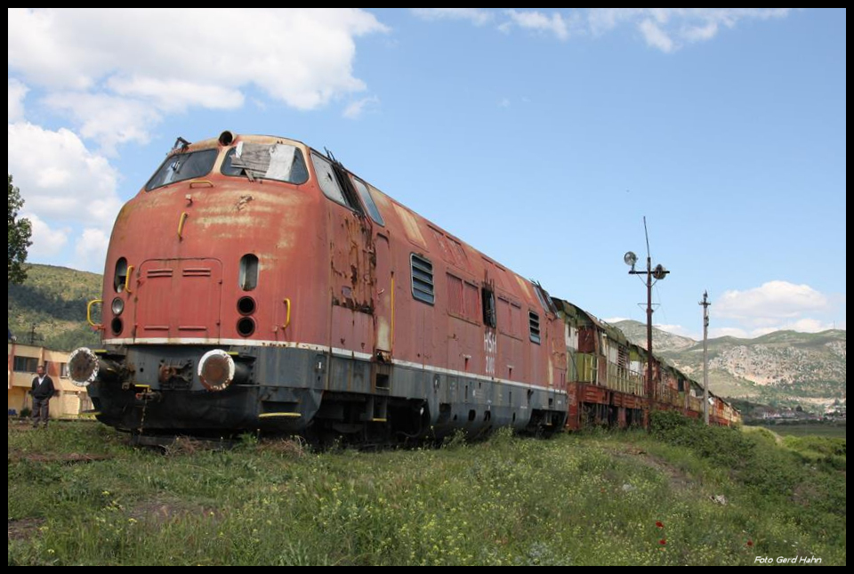 Albanien: Eine V 200.1 der DB zumindest gibt es hier am 18.5.2017 noch! HSH 2003 ex DB 200.124 steht fahrunfähig lädiert vor einem Lokzug, der ansonsten ausnahmslos aus tschechischen Cmellaks besteht, im Bahnhof Prrenjas nahe der mazedonischen Grenze. Es gibt dort zwar keinen Zugverkehr, aber der Bahnhof ist dennoch mit zwei Bahnern besetzt. Die netten Herren erklärten uns in aller Kürze den Verbleib der letzten V 200, die mit fünf an der Zahl 1989 nach Albanien kamen: Beim Umsturz mit der UCK kam es zu Übergriffen auf das Eisenbahn Gut.Zahlreiche Loks und Wagen wurden zerstört und später verschrottet. Die Lok HSH 2003 aber, die allein in Prrenjas stand, wurde dabei von dem Bahnhofsvorsteher und seinen Leuten heldenhaft verteidigt, so dass sie heute noch lediglich mit ein paar Einschüssen dort verblieben ist. Fahren wird sie sicher nicht mehr! Dazu fehlen zu viele Teile.