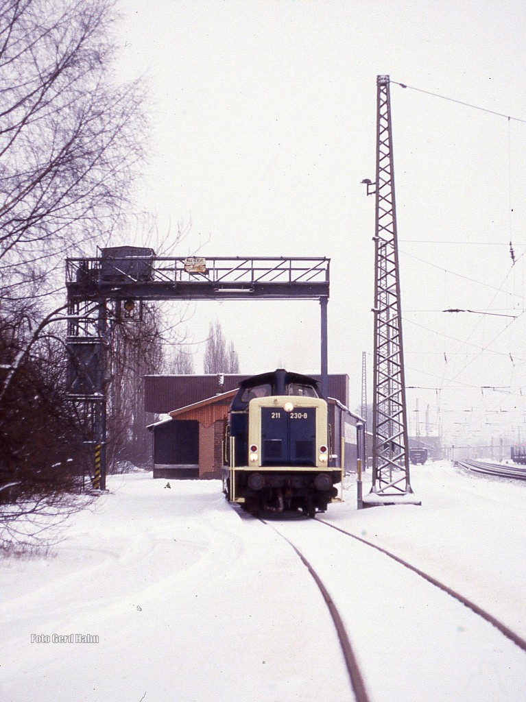 Alles Geschichte!!!
Am 12.11.1987, es war ein früher Wintertag, gab es noch im Bahnhof Hasbergen eine
Verladehalle und einen Kran mit Anschlussgleis. 211230 holte an diesem Tag um 15.15 Uhr wie üblich Wagen mit Düngemittelmaschinen der Amazone Werke ab. 
Heute sind alle Objekte verschwunden. Die Landwirtschaftsgeräte der Amazone werden mit dem LKW transportiert! Das Anschlussgleis ist abgebaut. Nur noch Spuren der Ladestraße sind vorhanden und der Mast für die  Rollbahn  steht noch an derselben Stelle. 