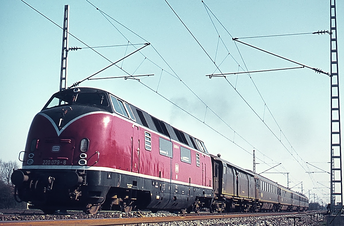 Als 220 079-8 im Februar 1975 bei Rheine nordwärts fährt, sind die Arbeiten zur Elektrifizierung der Strecke bis Salzbergen (und weiter zur niederländischen Grenze) bereits abgeschlossen, die Umstellung auf elektrischen Betrieb erfolgte zum Fahrplanwechsel Ende Mai. Genauso interessant wie die Lok ist die aus NS-Altbauwagen bestehende Zuggarnitur.