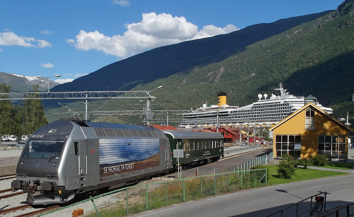 Als Reservelok ist am 20.08.2015 El 18 2245 in Flåm abgestellt. Rechts das Flåm Eisenbahnmuseum und im Hintergrund das Kreuzfahrtschiff Costa Fortuna.