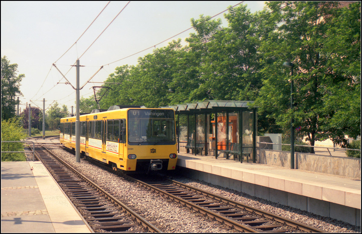Als die Stadtbahn Stuttgart noch jung war -

Mit der Umstellung der Linie 1 im Jahr 1986 entstand eine erste Neubaustrecke für die Stadtbahn. In Fellbach musste die Schleifenstrecke in der Innenstadt durch enge Straßen aufgegeben und eine neue Strecke entlang der der Esslinger und der Tainer Straße gebaut über die auf anderem Weg der gleiche Endpunkt an der Lutherkirche angefahren wird, wie zuvor die Straßenbahn auch. Die Erschließungswirkung der Fellbach Innenstadt hat sich aber dadurch verschlechtert, während dagegen die Schwabenlandhalle einen direkten Stadtbahnanschluss erhielt. 

Im Bild die Haltestelle 'Schwabenlandhalle' mit abweichendem Unterstand gegenüber den Standardhaltestellen in Stuttgart.

Scan vom Farbnegativ, vermutlich 1989 oder 1990, die Linienbezeichnung ist schon 'U1' 
