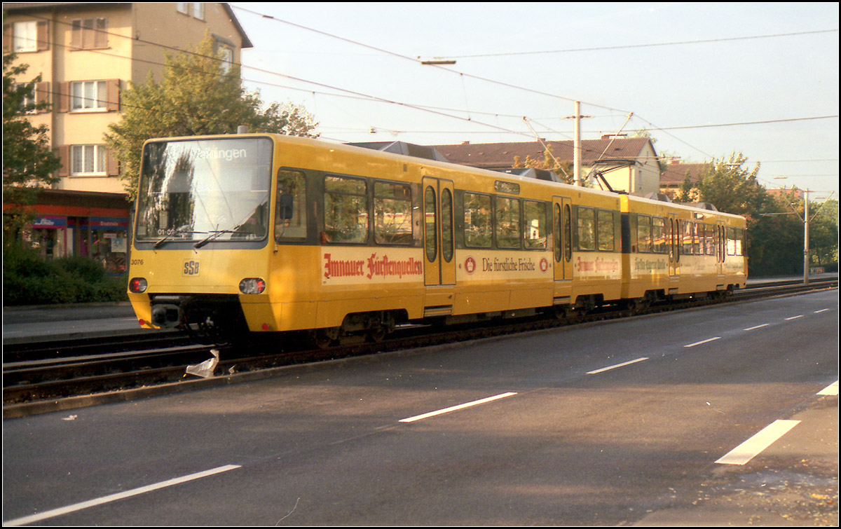 Als die Stuttgarter Stadtbahn noch jung war -

Der S-DT 8 ist ein achtachsiger Doppeltriebwagen mit Antrieb auf allen Achsen aufgrund der Stuttgarter Steilstrecken. Ursprünglich für die maximale Steigung von 7% gebaut, schaffte er aber auch die Steilstrecke zum Eugensplatz mit 8,5%. Gebaut wurden die Stadtbahnwagen der ersten Serien von DUEWAG.

Ursprünglich war für die U-Bahn Stuttgart ebenfalls ein achtachsiger Doppeltriebwagen ähnlicher der Münchner Typen A oder B mit einer Breite von 2,90 Meter für Stromschienenbetrieb geplant. Als die U-Bahnplanungen auf das Stadtbahnkonzept reduziert wurden, wurde die Bauart Doppeltriebwagen beibehalten, aber auf die maximale Breite für Strecken im Straßenraum auf 2,65 Meter festgelegt. Dabei entspricht ein S-DT 8 von der Länge von 38,8 Meter in etwa der Länge einer Doppeltraktion des GT 4-Straßenbahnwagens. Dies war von Bedeutung für die Weiternutzung bestehender Betriebshöfe bzw. Hauptwerkstatt. Die Abmessungen und Bauart entspricht dabei auch dem nie gebauten Stadtbahnwagen A für die Stadtbahn Rhein-Ruhr. Dort wurde dann der flexiblere Stadtbahnwagen B, ein 6achsiger Gelenktriebwagen zum Standardfahrzeug der ausgebauten Stadtbahnstrecken.

Das Fahrzeug ist als Sitzplatzfahrzeug gestaltet, das heißt es gibt nur zwei Türen pro Wagen und Seite. Bei der Münchner U-Bahn sind es drei. Dies ging hier aber auch nicht anders, wären doch bei einer Türanordnung analog zu München die Drehgestellbereiche im Weg, waren doch Anfangs noch Klapptrittstufen notwendig. Die Innenraumaufteilung wirkt aber auch heute sehr aufgeräumt und übersichtlich, ganz anders als bei vielen Niederflurbahnen, wo immer irgendwie die Fahrwerke in den Fahrgastraum reichen.

Ich kenne eigentlich kein straßenbahnähnliches System sonst in der Welt, das mit Doppeltriebwagen betrieben wird. Dabei gibt es etliche Nachteile: Das Fahrzeug ist recht ungelenkig und braucht einen Bogenhalbmesser von 50 Meter, der Stadtbahnwagen B nur 25 Meter. Das hat dann dazu geführt, dass das ganze Streckennetz neben der Umsprung von Meter- auf Normalspur auch von der Trassierung her angepasst werden musste, was beispielsweise zum Wegfall der kurvenreichen Strecke über den Botnanger Sattel zur Folge hatte mit Ersatz durch einen Tunnel. Anderseits ergab sich durch diesen Sachzwang auch eine Erhöhung der Reisegeschwindigkeit, was auch im Zusammenhang mit der in Stuttgart recht gut funktionierenden Vorrangschaltung an Lichtsignalen zu sehen ist. Anderseits führt die recht das recht schnelle Fahren auch häufig zu Unfällen mit Fußgängern oder Autos.

Anfangs wurde etliche Straßenbahnstrecken, die nur schwer umrüstbar waren, stillgelegt (zuletzt 1994 nach Obertürkheim.) Inzwischen wurde man pragmatischer und früher hätte man nie gedacht, dass einmal auch über die Gänsheide-Strecke zur Ruhrbank mit den Stadtbahn-Triebwagen gefahren wird. Ganz besonders interessant ist es dann wenn aufgrund von Umleitungen die U7 über diese Strecke geleitet wird und die 80 Meter langen Zügen ohne Halt auf der steilen Straße unterwegs sind.

Auch Neubaustrecken sind eher schwierig umzusetzen, gerade in engen Ortsdurchfahrt. Hier wird dann schnell ein Tunnel gebraucht. Ludwigsburg verzichtet daher auch auf eine Ausdehnung der Stuttgart Stadtbahn in ihre Stadt und plant sinnigerweise eine Niederflurstraßenbahn.

Im Bild der S-DT 8 3075/76 aus der ersten Serie der Baujahre 1985-86 als U1 in der Nürnberger Straße in Bad Cannstatt.

Scan vom Farbnegativ, Ende der 1980iger Jahre

