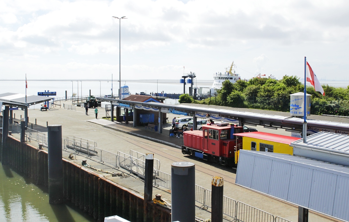 Am 03.07.2021 ist die Lok  Aurich  mit abreisenden Urlaubern im Borkum Reede angekommen, im Hintergrund lugt die AG Ems-Fähre  Groningerlanden  nach Eemshaven/Niederlande zwischen den Büschen hervor
