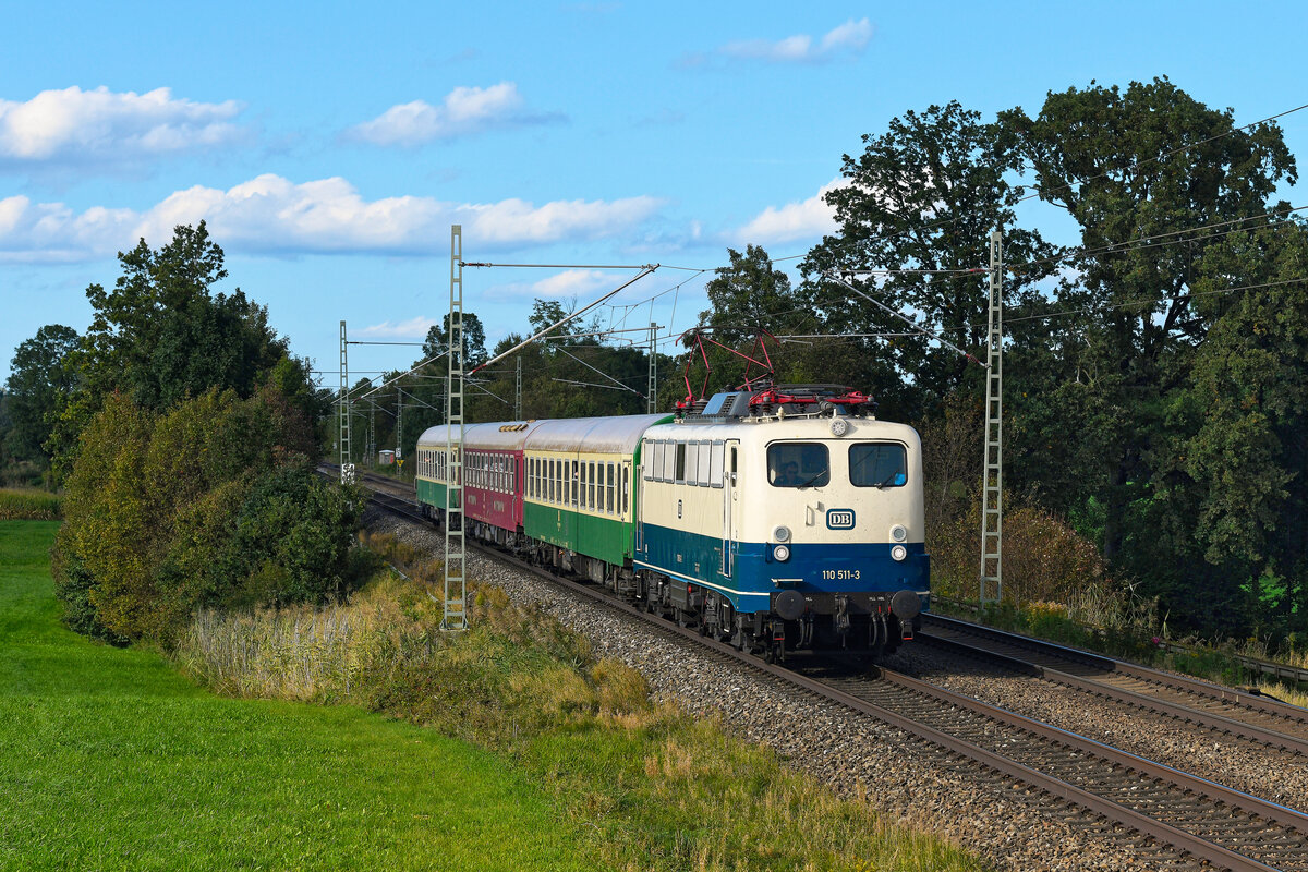 Am 04. Oktober 2023 verkehrte im Auftrag des Erzgebirgsstübls Dorfchemnitz ein Sonderzug mit der Zugnummer DPE 1820 von Chemnitz nach Rosenheim. Als Zuglok wurde die mustergültig in den Zustand der Epoche IV zurückversetzte 110 511 der Pressnitztalbahn verwendet. Die Lok hat eine bewegte Geschichte hinter sich. Ursprünglich im Jahre 1959 von Siemens und Krauss-Maffei als 139 134 an die Deutsche Bundesbahn ausgeliefert, wurde sie Mitte der 1980-er Jahre durch eine Änderung der Getriebeübersetzung zu einer Lok der Baureihe 110 umgebaut. Darüber hinaus erhielt sie im AW Opladen den damals üblichen ozeanblau-beigen Neulack und die höchste jemals bei der Baureihe 110 verwendete Ordnungsnummer. Das war insofern bemerkenswert, da ja alle Loks der Baureihe ab der Ordnungsnummer 288 den markanten windschnittigeren Lokkasten mit der  Bügelfalte  besaßen. Hintergrund für diese Maßnahme war ein damaliger Mangel an Schnellzugloks. Danach kam sie primär in Nordrhein-Westfalen zum Einsatz. 2005 erhielt sie eine Lackierung in weiß mit roten Streifen und wurde vom AW Dessau als Gewährleistungslok eingesetzt. Acht Jahre später wurde 110 511 an die Pressnitztalbahn verkauft, erhielt eine blaue Lackierung und wurde primär im Güterverkehr genutzt. Die Umgestaltung in das klassische Erscheinungsbild der DB aus den 1970-er und 1980-er Jahre erfolgte 2022. Seitdem ist die  Kastenzehner  primär vor Autotransportzügen von und nach Emden zu sehen. So war natürlich die Freude groß, diese interessante Lok auch mal im südlichen Bayern zu sehen. Mit den drei ebenfalls in den Zustand der 1980-er Jahre zurückversetzten  Halberstädtern  konnte man sich der Illusion hingeben, man hätte einen klassischen, wenn auch kurzen Interzonenzug, vor sich. Wie so oft machte es das Wetter spannend, am ehemaligen Block Hilperting hatte die Sonne bei Durchfahrt des Sonderzuges allerdings halbwegs ein Einsehen und leuchtete die Szenerie zumindest teilweise aus.  