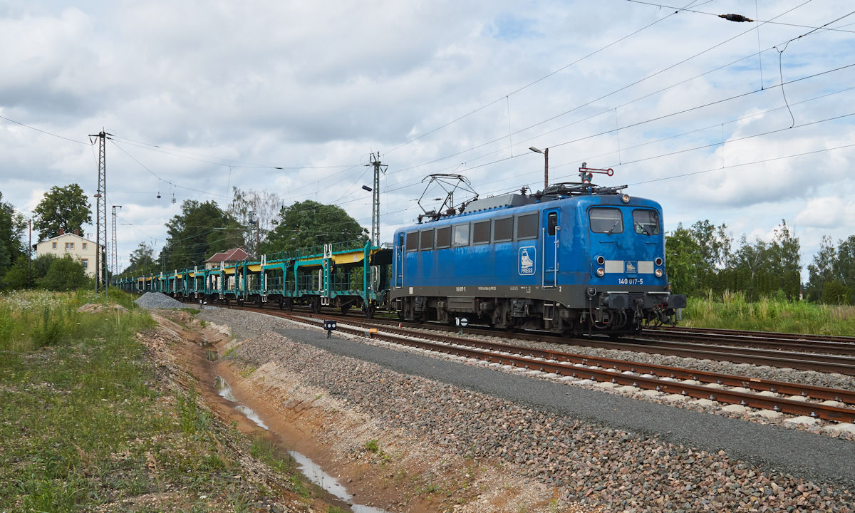 Am 07.07.2021 zog 140 017 einen leeren Autozug durch Regis-Breitingen in Richtung Süden. Der Bahnhof hat seit 1990 seine einst umfangreichen Gleisanlagen verloren und wird bald auch das Flügelsignal verlieren.