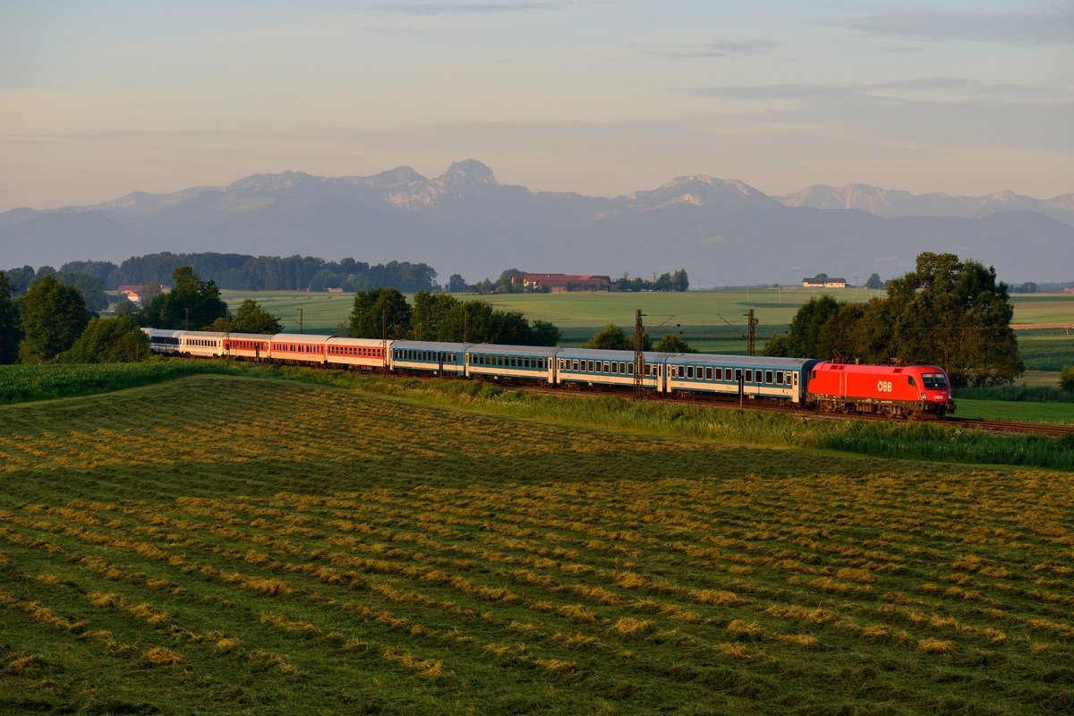 Am 08. Juli 2016 stand ich erneut früh auf, um noch eine Motiv-Variation des zwischen Salzburg und München vereinigt verkehrenden EN 462 / EN 498 bei Haus aufzunehmen. Diesmal wurde mehr Brennweite verwendet. An diesem Tag beförderte 1116.113 den aus Wagen dreier Bahnverwaltungen gebildeten Zug, der gerade von den ersten Sonnenstrahlen ausgeleuchtet wird.
 