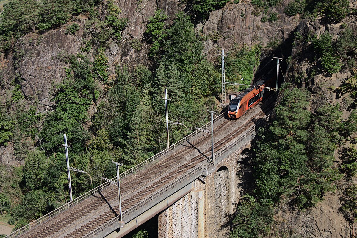 Am 08.08.2026 f�hrt dieser Traverso der SOB gerade �ber die Ch�rstelenbachbr�cke in den kurzen Tunnel vor Amsteg Silenen in Richtung Altdorf. Diese Z�ge sind inzwischen Standard auf der Panoramastrecke.  
Aufgenommen habe ich das Bild von einer Kehre der engen Strasse nach Bristen im Maderandertal. 