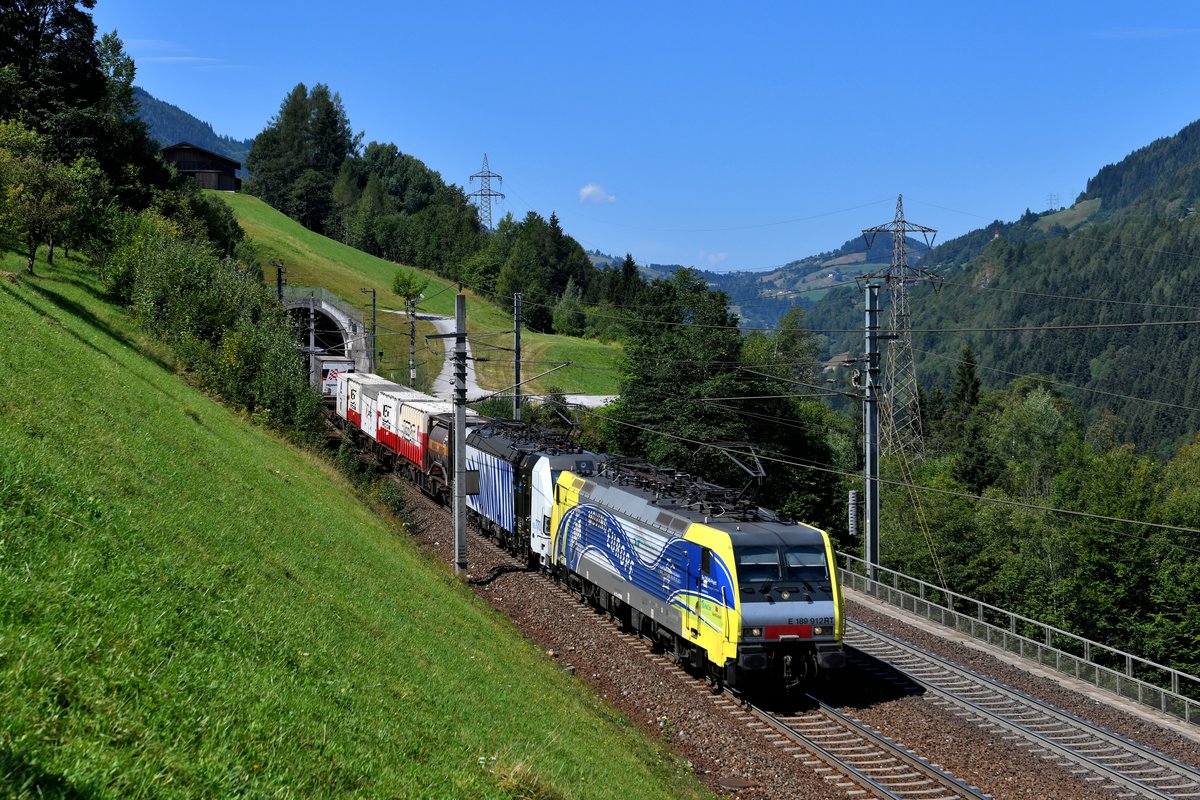 Am 09. August 2018 konnte ich die 189 912 und 193 770 von Lokomotion mit einem aufgrund der Brennersperre umgeleiteten KLV bei Oberuntersberg in der Nähe des Bahnhofs Loifarn an der Tauernbahn aufnehmen. Hier sieht man den Zug beim Verlassen des Kenlach-Tunnels, die Strecke wurde in diesem Bereich vor einigen Jahren komplett neu trassiert. 