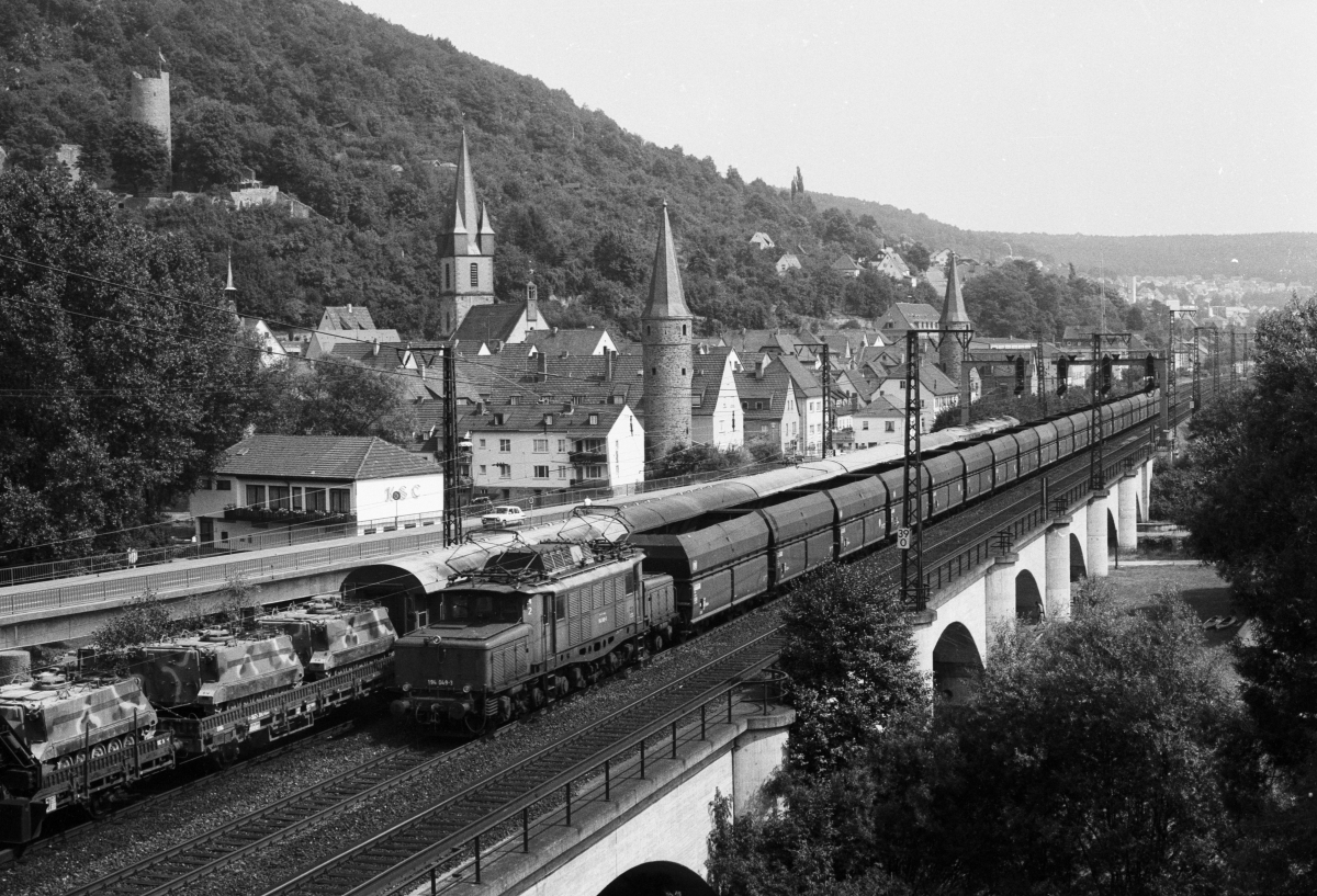 Am 10.8.1983 ist 194 049 mit einem Leerzug aus Selbstentladewagen vor der markanten Kulisse von Gemnden/Main unterwegs.
