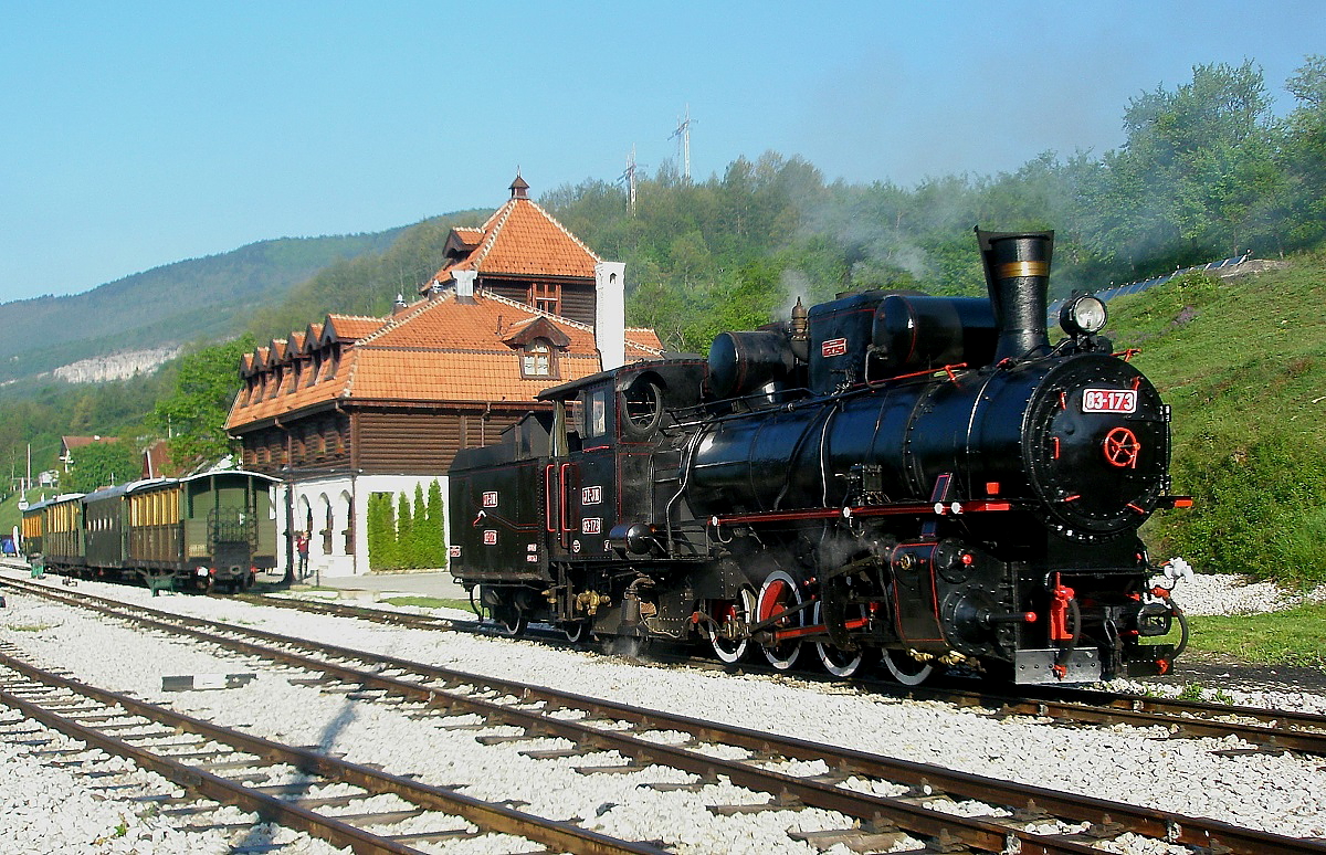 Am 11.05.2009 steht 83-173 der Museumsbahn Mokra Gora von der Morgensonne angeleuchtet im Bahnhof Mokra Gora, dahinter das kurz zuvor eröffnete Hotel. Bei dieser Bahn handelt es sich um ein wieder aufgebautes Teilstück der einstigen 760 mm-Strecke von Beograd nach Sarajevo und zur Adria. Zwischen Mokra Gora und dem  Scheiteltunnel sind nur wenige km Luftlinie, jedoch 240 m Höhe zu überwinden. Dies war ohne Zahnstange nur durch eine entsprechende Schleifenentwicklung und zahlreiche Tunnel möglich, insgesamt liegen fünf Ebenen der Strecke übereinander. 