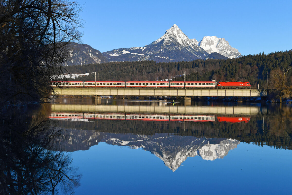 Am 12. Februar 2022 brachte die 1216.011 den EC 83 von München HBF nach Verona P.N. und konnte bei Langkampfen im unteren Inntal fotografiert werden. Der ruhig dahinfließende Inn ermöglichte eine Spiegelung des internationalen Fernzugs samt dahinter liegendem Gebirge.