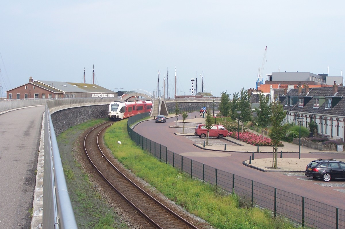 Am 14.8.15 hat ein GTW 2/8 von Arriva eben den Bahnsteig von Harlingen /Frysl. verlassen. Die Aufnahme entstand von der Schutzmauer, die den Hafen gegen Flut und Hochwasser schützt und gleichzeitig einen Radweg trägt.