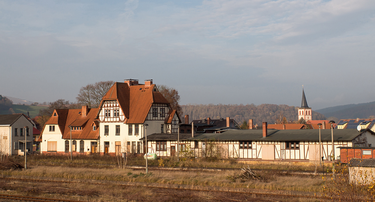 Am 15.11.14 habe ich wieder dem stillgelegten Bahnhof des schönen Städtchens Vacha einen Besuch abgestattet.
Vacha befindet sich an der ehemaligen innerdeutschen Grenze; die Werra trennt Thüringen und Hessen. Die westlichste Stadt Thüringens ist Endpunkt der Strecke Bad Salzungen - Vacha.
Bis nach dem 2. Weltkrieg fuhren Reisezüge noch weiter bis nach Philipsthal, durch die spätere Grenzschließung wurde dieser Streckenabschnitt jedoch teilweise rückgebaut. So endete der Reisezugverkehr an der innerdeutschen Grenzstadt.
Nur der Kaliverkehr befuhr bis 1999 die Strecke weiter bis nach Unterbreizbach. Man setzte hierfür anfangs die BR 44, welche in den siebziger Jahren durch die BR 120 (Taigatrommel) abgelöst wurde, später die BR 131/231, und letztlich die BR 232 auf diesem steigungsreichen Streckenabschnitt ein.
Links im gezeigten Bild ragt ein kleiner Teil eines der Abraumberge hervor.

 Das Land Thüringen bestellte den Personenverkehr zwischen Bad Salzungen und Vacha zum 10. Juni 2001 ab. Grund hierfür war der Busparallelverkehr, der durch den Wartburgkreis finanziert wurde. In der Zeit vom 1. Januar bis zum 10. Juni 2001 wickelte noch die Süd-Thüringen-Bahn den Verkehr im Auftrag der Deutschen Bahn AG ab. Mit der Einstellung der Holzverladung im Bahnhof Dorndorf Ende 2001 endete der Gesamtverkehr. Eine letzte Befahrung der Strecke fand am 30. Dezember 2002 durch einen SKL der DB AG statt, bevor mit der Stilllegung zum 31. Dezember 2003 ein vorläufiger Schlussstrich gezogen wurde.  (Quelle: Wikipedia) [de.wikipedia.org]

Nichts ist mehr los im Bahnhof Vacha - und das seit fast 14 Jahren... .
Eine beherzte, private IG erneuerte noch vor 3 Jahren ein paar Güterzuggleise, incl. eines, welches über den beschrankten Bü führt.
Doch nichts ist geblieben – leider - genausowenig die Umsetzung der geplanten Holzverladung in Vacha, gemäß eines Vorhabens aus dem Jahr 2007.

Aber es gibt streckenmäßig aus den letzten Jahren auch Positives zu berichten. So startete am 27.08.2011 der Probebetrieb zum Sägewerk der Aloysius Krenzer KG in Dorndorf, ein Ort vor Vacha. Mittlerweile findet neben des bestehenden Güter-Anschlußverkehres nach Merkers nun auch wieder regelmäßiger Holzverkehr auf der Strecke nach Bad Salzungen statt.

Anmerkung: Der Vachaer Kirchturm ist in Natura leicht schief.
