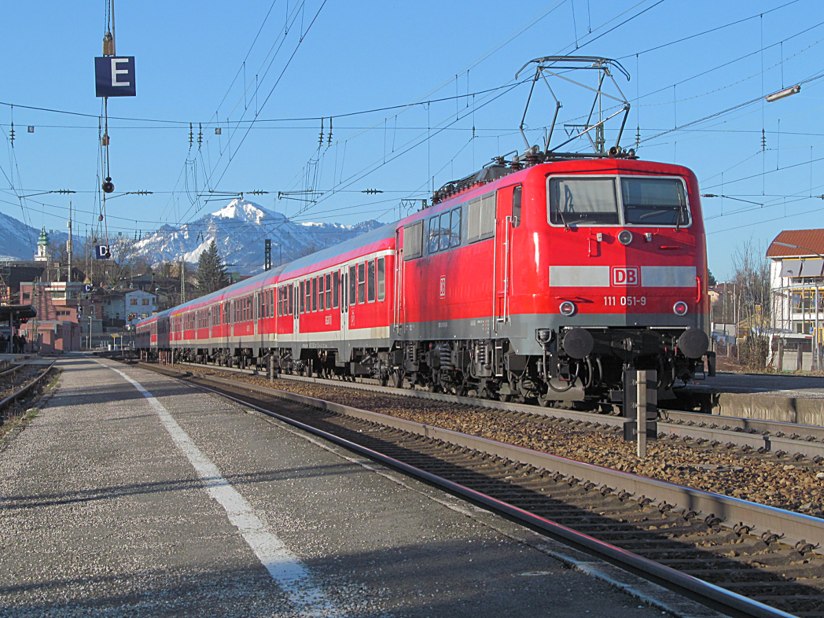 Am 16. März 2012 gab es einen besonders klaren Wintermorgen. Lok 111 051 wartet um 7.47 Uhr mit einem Regionalexpress nach München im Bahnhof Traunstein vor eindrucksvoller Bergkulisse auf Abfahrt. Wegen des Berufsverkehrs besteht der Zug aus acht Waggons. Heute verkehrt hier der Meridian und der Bahnhof wurde gründlich umgebaut.