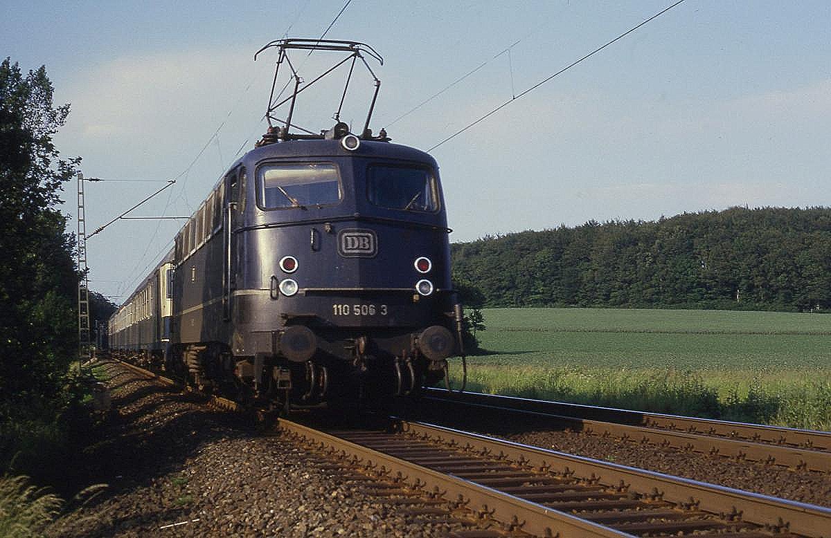 Am 1.7.1987 ist um 18.55 Uhr am Ortsrand von Hasbergen die blaue 110506 mit dem Nachverkehrszug nach Münster unterwegs.