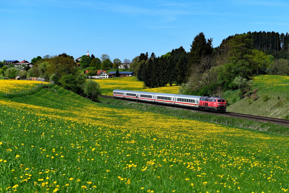 Am 27. April 2018 war die 218 343 für die Beförderung des IC 2084  Nebelhorn  nach Hamburg Altona eingeteilt. Sie wird diesen Zug bis Augsburg bespannen. Bei Aitrang konnte ich den Fernzug inmitten des blühenden Löwenzahns fotografieren. Im Hintergrund erkennt man die Ortschaft Görwangs. 