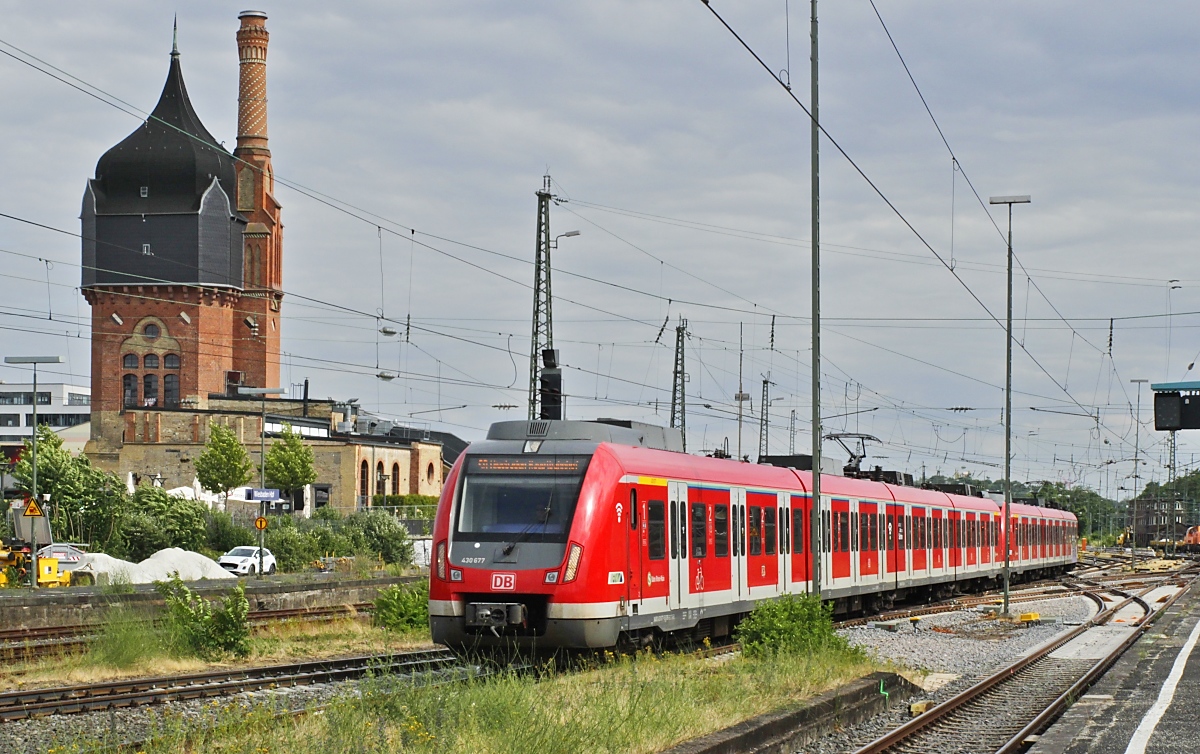 Am 27.06.2023 fahren 430 677 und ein weiterer 430 mit einer S-Bahn im Hauptbahnhof Wiesbaden ein. Der im Hintergrund sichtbare, 1897/99 errichtete und heute unter Denkmalschutz stehende 36 m hohe Wasserturm ist ein Überbleibsel des 1991/92 stillgelegten Vieh- und Schlachthofes. In den Turm wurde der Schornstein der Maschinenhalle integriert.