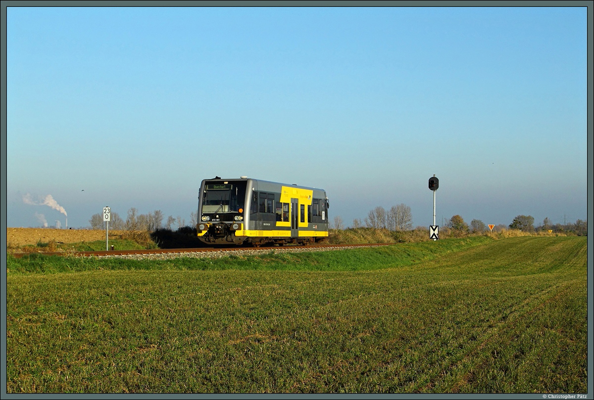 Am 28.10.2014 rollt 672 901 der Burgenlandbahn bei Langeneichstädt als RB 34819 vorbei an abgeernteten Feldern Richtung Querfurt. Der Bahnhof Langeneichstädt weist eines der letzten noch in Betrieb befindlichen EZMG-Stellwerke Deutschlands auf. Diese Stellwerksbauform wurde ab 1976 von der DR aus der UdSSR importiert um den Betrieb auf Nebenbahnen zu rationalisieren. Im Bild zu sehen ist das markante Einfahrvorsignal des Bahnhofs. Im Hintergrund das Braunkohlekraftwerk Schkopau.