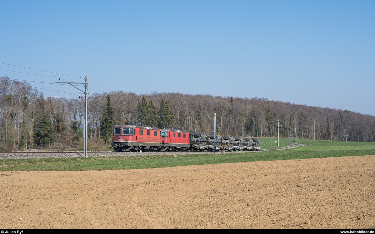 Am 29. März 2019 brachten die Re 4/4 II 11306 und 11263 einen Panzertransport von Biel RB nach Bure. Auf der ausschliesslich Militärtransporten dienenden Strecke zwischen Courtemaîche und Bure verkehrte der Zug aufgrund der grossen Steigung von bis zu 45 ‰ in drei Teilen.<br>
Hier zu sehen ist der erste Zugteil kurz vor der Einfahrt in den Bahnhof Bure.